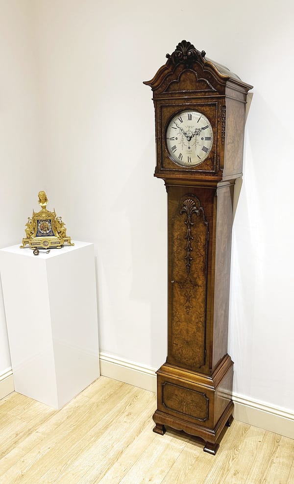 london-walnut-quarter-chiming-longcase-grandfather-clock-showroom-view A high quality, small proportioned, Westminster chiming longcase / grandfather clock by Maple of London. Image of the clock in a showroom setting next to a french mantel clock